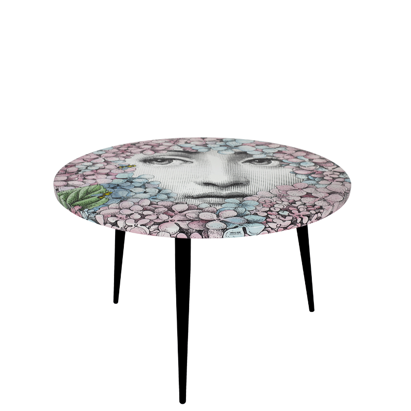TABLE ORTENSIA. THE ROUND¬†TABLE¬†IS DRESSED WITH THE D√âCOR ORTENSIA (HYDRANGEA), A RECENT REINVENTION BY BARNABAFORNASETTI. THIS MOTIF ENRICHES THE SERIES TEMA E VARIAZION (THEME AND VARIATIONS) WITH A REINTERPRETATION OF LINA CAVALIERI ICONIC FACE PEEKING AT THE OBSERVERS BEHIND COLOURFUL AND JOYFUL HYDRAGEAS, THE SAME PLANTS THAT HAVE SURROUNDED CASA FORNASETTI IN MILAN FOR 60 YEARS. THE TABLE IS PRINTED, LACQUERED AND PAINTED BY HAND.
