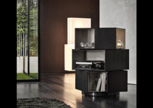 PAGE by RODOLFO DORDONI, designed in 2019. With its decidedly sculptural presence and the contrasting textures of the interiors and exteriors of its three volumes, the page bookcase is inspired by works of modern art. Its misaligned blocks, set one on top of the other also call to mind contemporary architectures. Fully swivelling, it is characterised by volumes in the form of parallelepipeds, with outer edges in mocha-coloured wenge wood and glossy painted warm grey-coloured interiors, and it stands on a circular base with a glossy pewter-coloured finish. A bold piece of furniture that is sure to turn heads, ideal in any part of the room, including the centre. In addition to its function as a bookcase, page can also be used as a contemporary display cabinet to accommodate objects or as a bar cabinet.