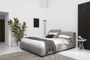 PORTLAND bed designed by Daniele Lo Scalzo Moscheri. The idea underpinning this product comes from reclaimed padded seats from exclusive luxury vintage trains and features soft vertical quilting that tempers the grandeur of the generously voluminous design. When the headboard is opened, PORTLAND offers a practical functional container unit for storage. The item is available with three versions of the feet in wood and one in metal with the option of choosing the look and height from the ground that suits the customer best. The PORTLAND bed is available with a fixed bed base or container unit. Can be upholstered in fabric or leather.