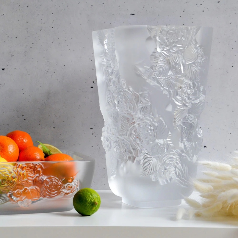 PIVOINES vase. Alliance of brute strength and delicacy, juxtaposition of square shape to the curved lines of the sculpted motifs, the PIVOINES vases and bowl embody a contrast of mineral strength and floral romanticism. Symbol of prosperity, beauty and honour, the peony is an emblematic flower, especially in China where it is often depicted. As if carved in the gouge of a rock garlands of flowers take possession of crystal, like luxuriant nature takes its rightful place over abandoned constructions. Their modelling also evokes the process of Lost Wax sculpture, when the craftsman breaks the plaster mould to reveal the piece.
