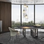 WEDGE DINING TABLE by NENDO, designed in 2019. WEDGE explores the concept of a table with a strong graphic style, offering both a dining room and coffee table version. In the dining table, the bulky look created by the solid sculptural masses of the semi-circular legs of wedge contrasts with the lightweight feet, which culminate in an oblique chisel tip shape. The entire volume of the table, hosting the large top, appears to become weightless and leans lightly on the tips of the legs, challenging the law of gravity. The element of surprise is even stronger in the version with barrel-shaped glass top, the surface of which reveals the semi-circles of the supports, positioned in a purposely irregular formation.